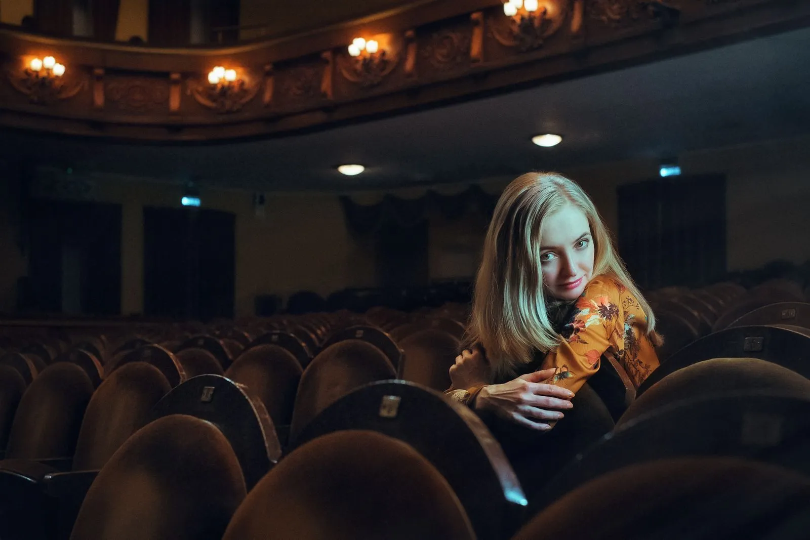 Young woman posing elegantly in an empty theater, exuding charm and poise.